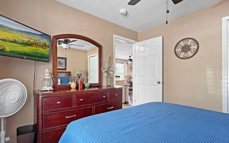 A bedroom with a bed , dresser , mirror and ceiling fan