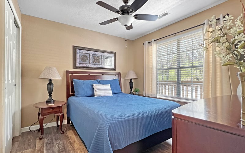 A bedroom with a bed , dresser , lamps and a ceiling fan.