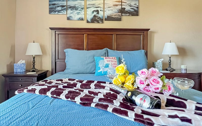 A bedroom with a bed , nightstands , lamps and a bottle of wine on the bed.