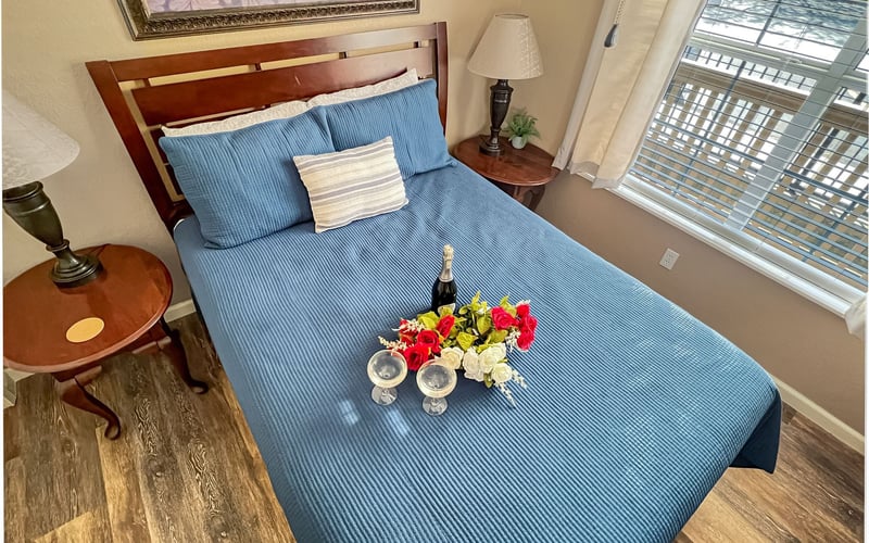 A bedroom with a bed , two lamps , a vase of flowers and a bottle of wine.