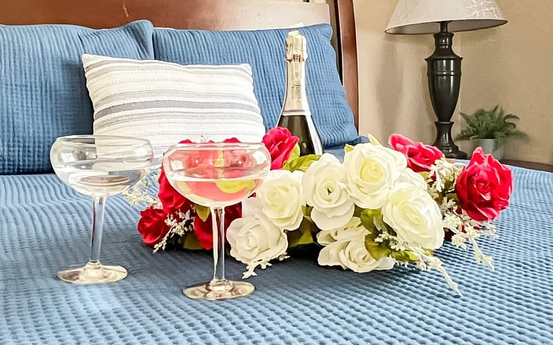A bed with a bottle of champagne , two glasses of wine and flowers on it.