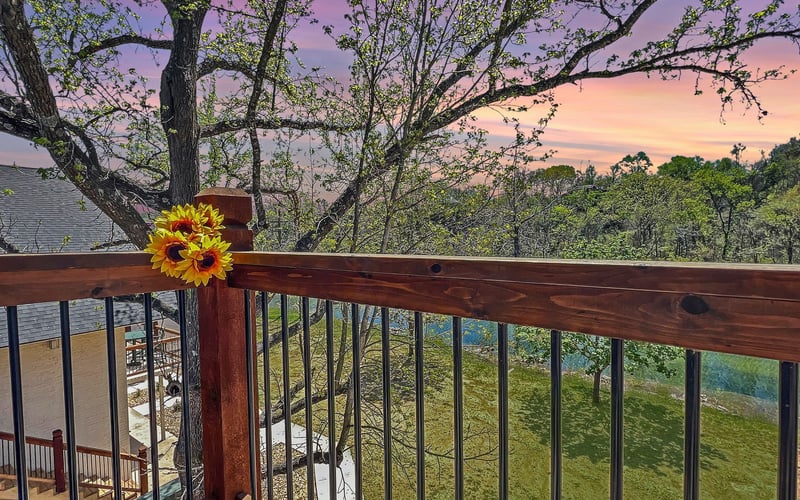 A wooden deck with a sunflower on the railing at sunset.